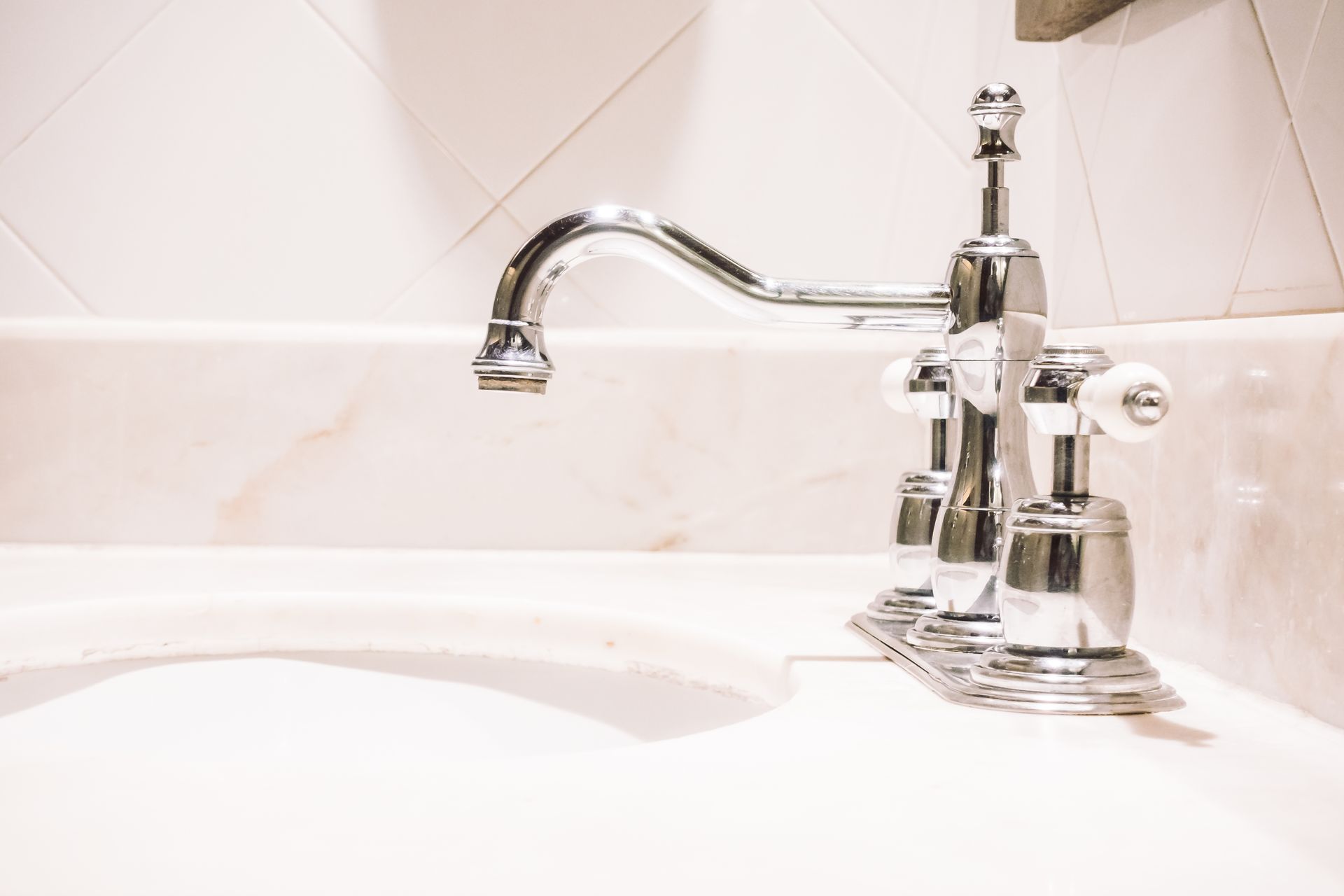 Chrome faucet over a white sink, in a white tiled bathroom.