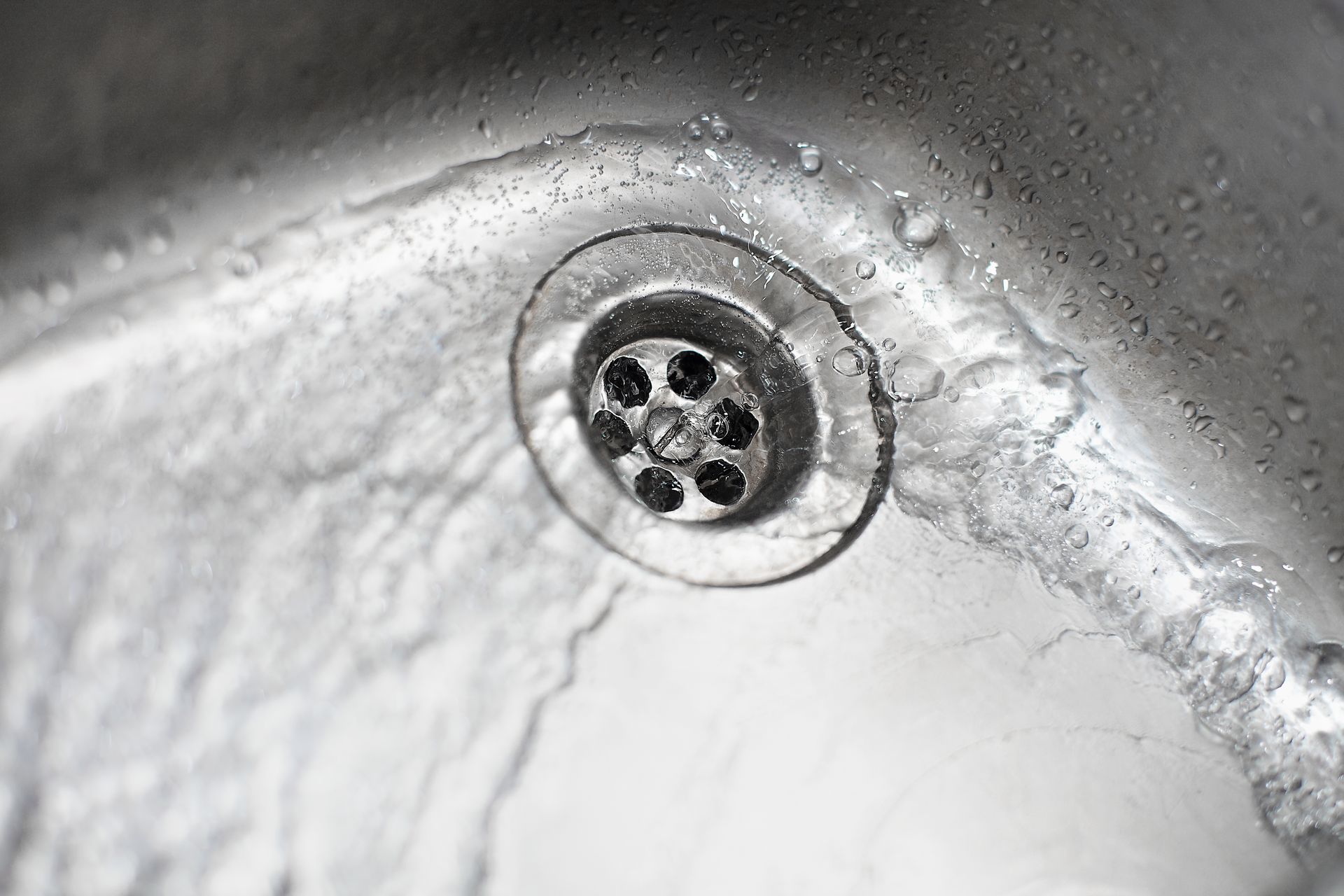 Water flowing into a stainless steel sink, over and around a drain.