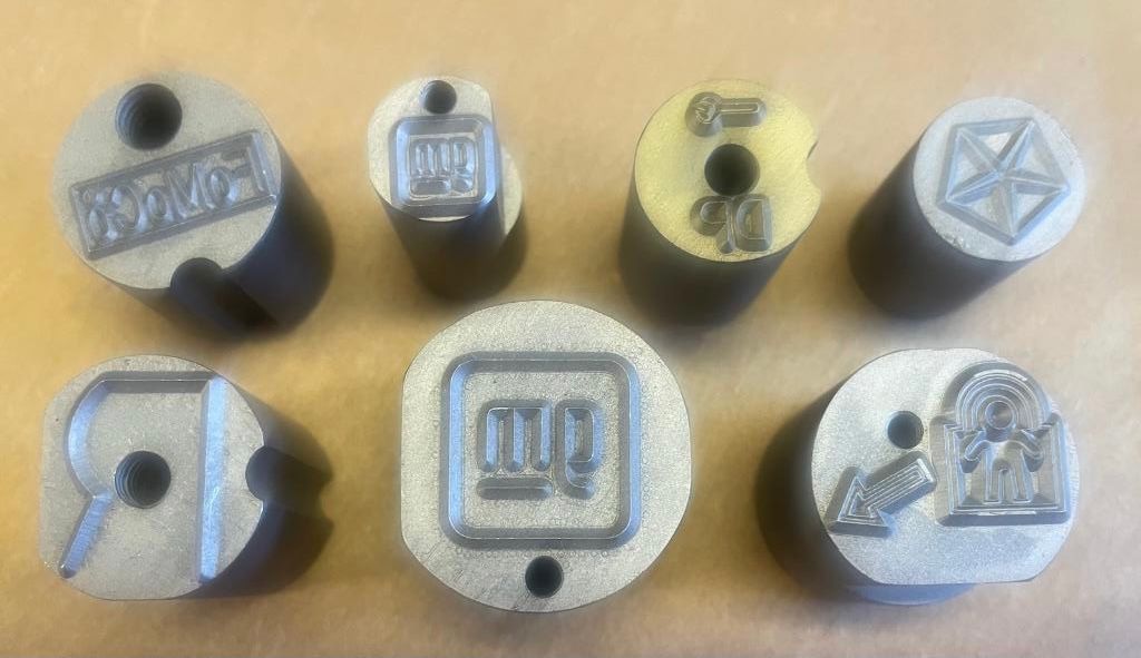 Close-up of seven metal stamps with various geometric shapes and text designs.