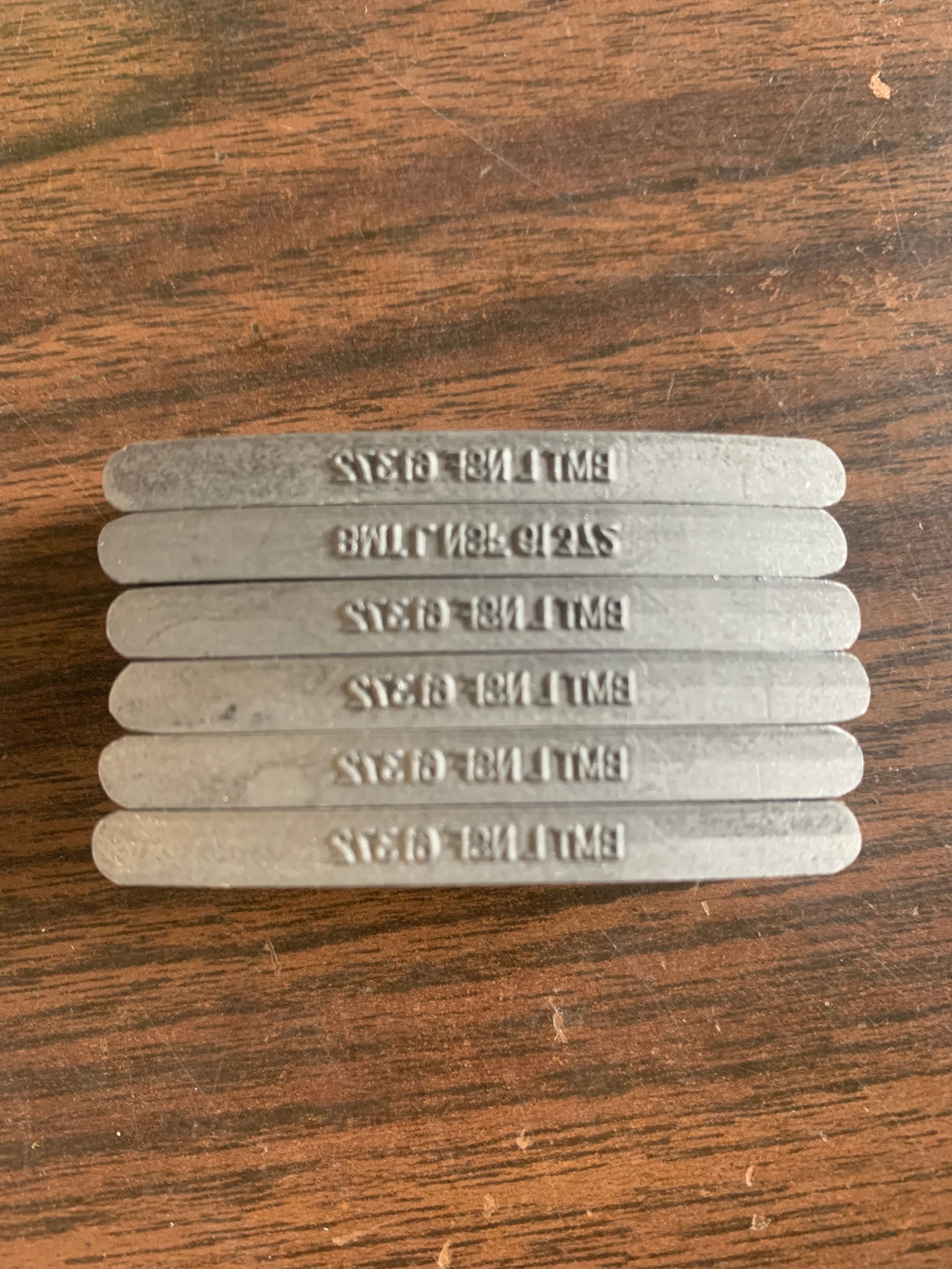 Seven silver bars stacked on a wooden surface, each inscribed with 