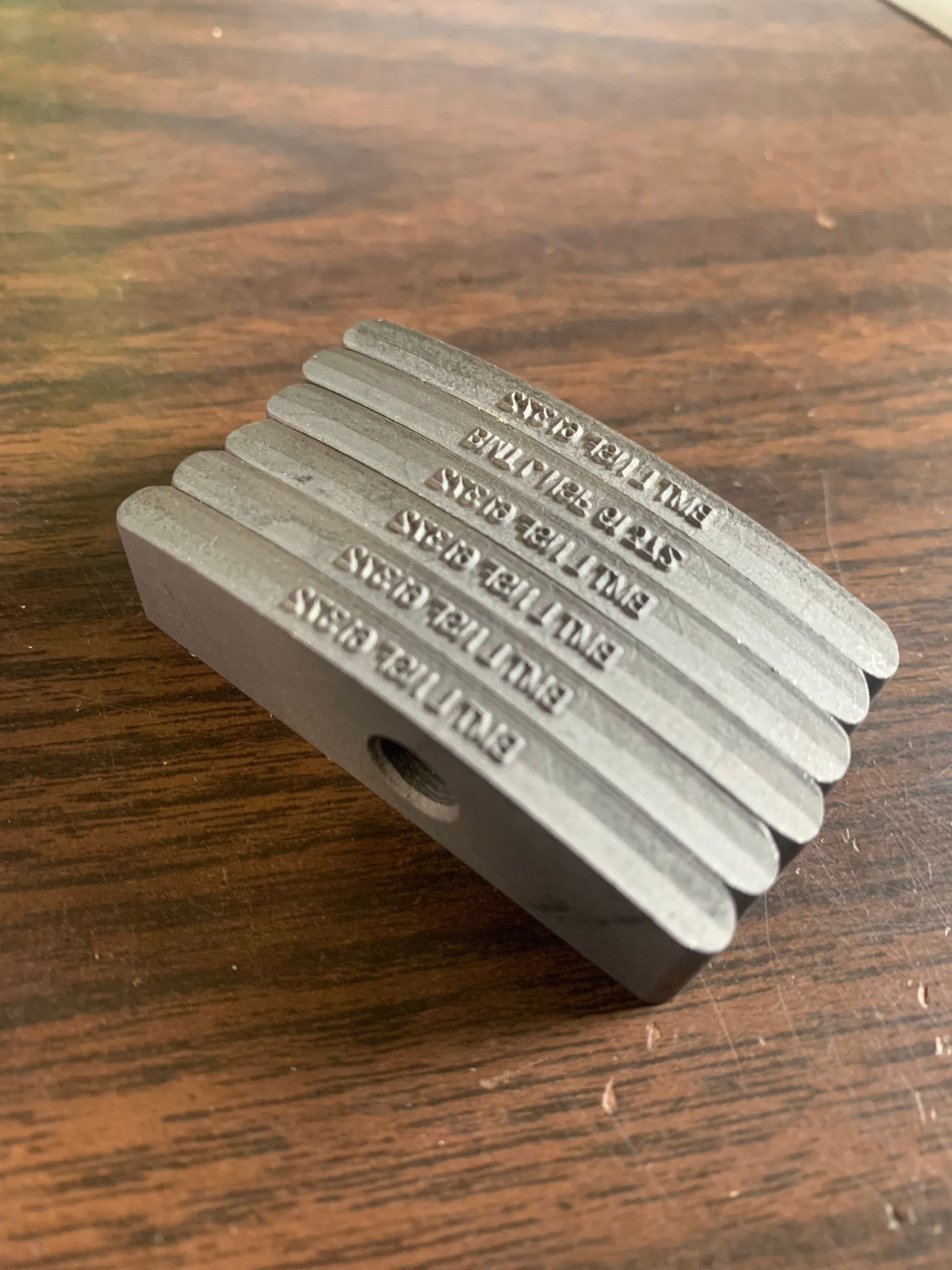 Gray metal grooved part with text etched into each groove.