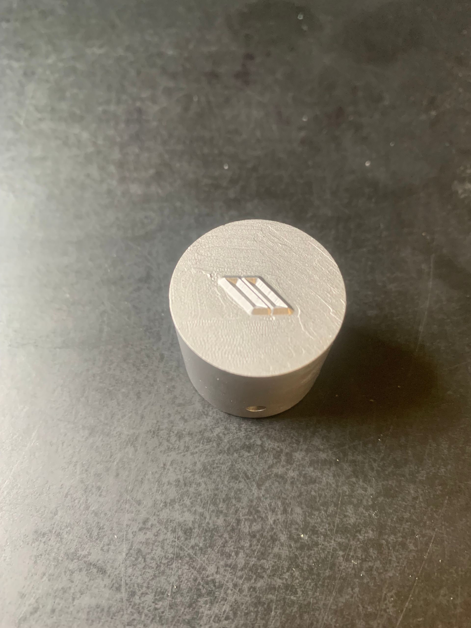 Gray cylindrical knob with a white, stylized 