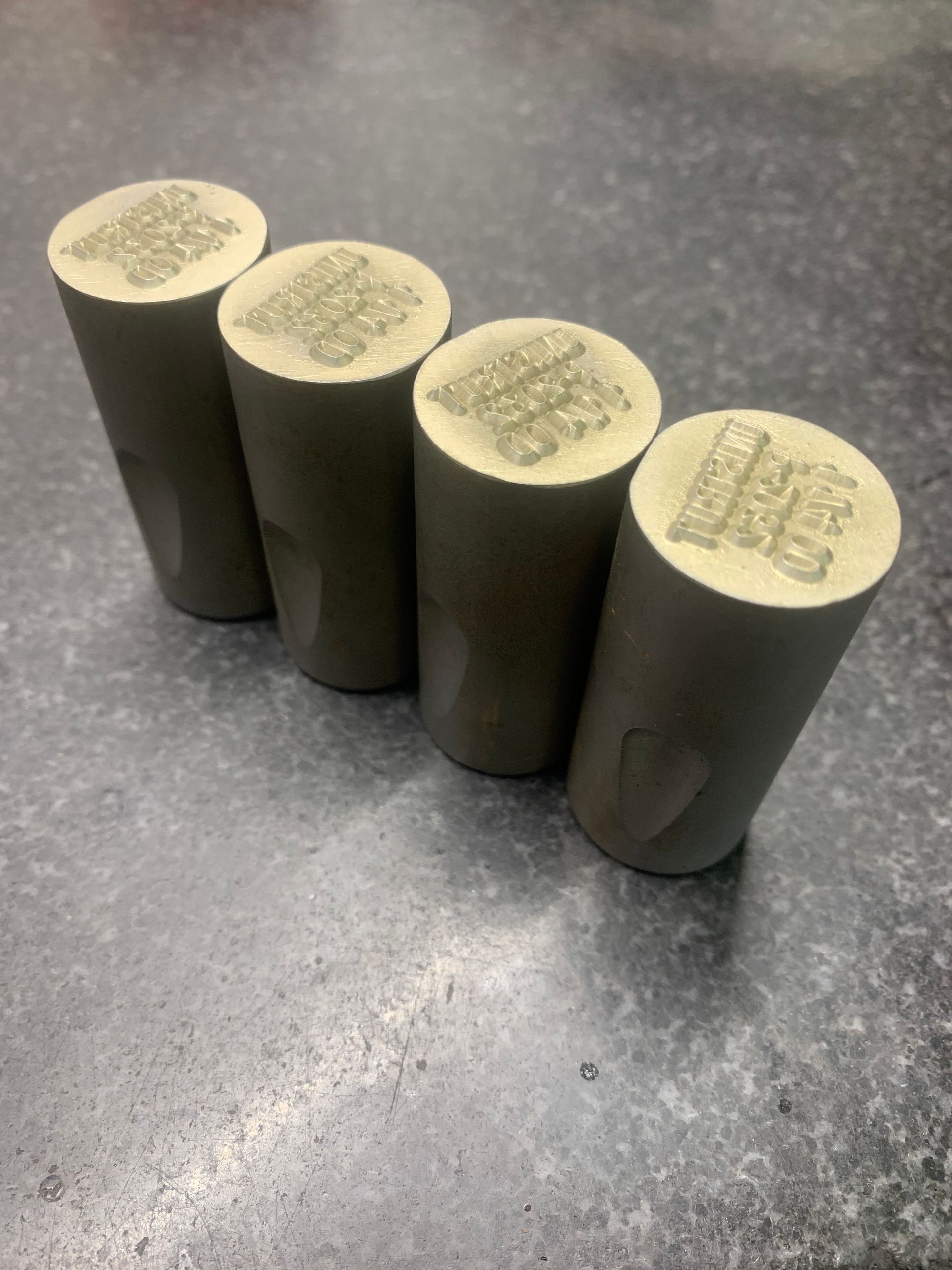 Four cylindrical, light-colored concrete test cylinders with stamped markings sit on a gray surface.