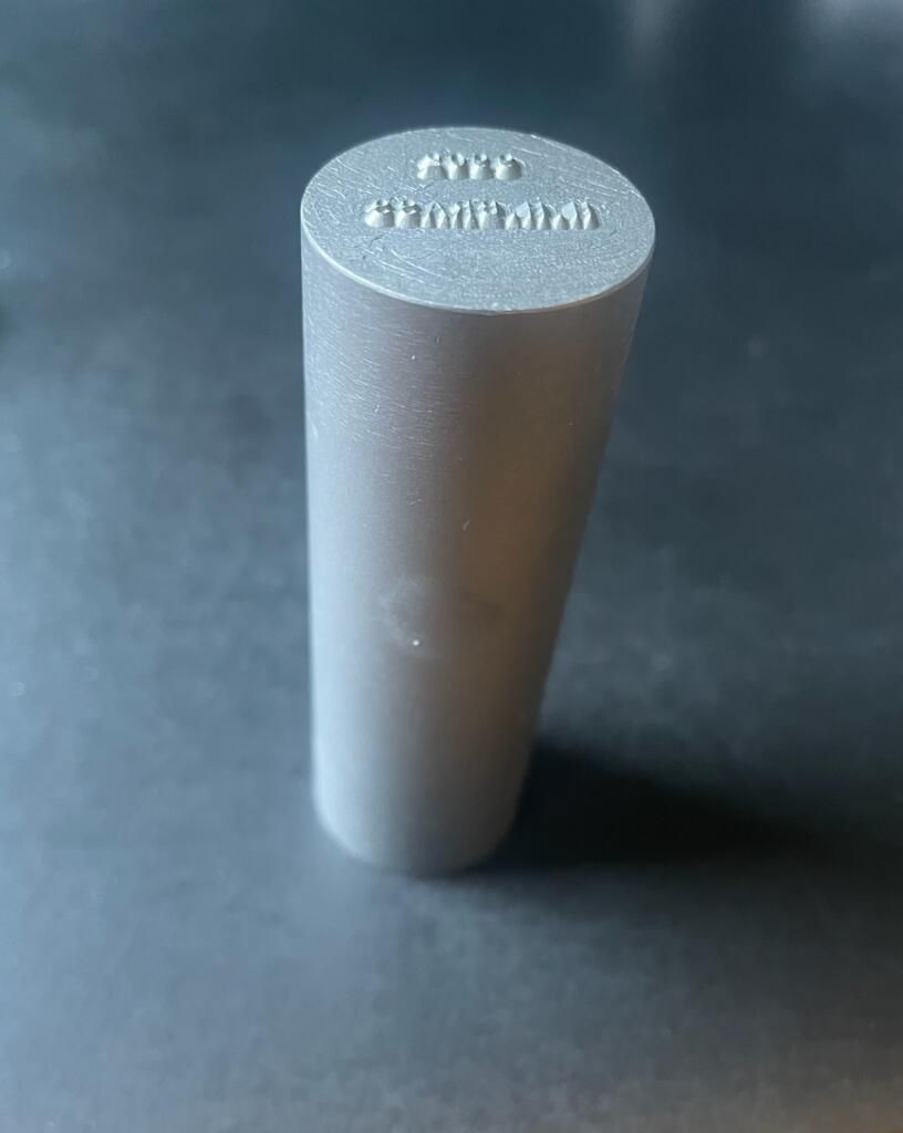 Silver cylinder with engraved text on the top.