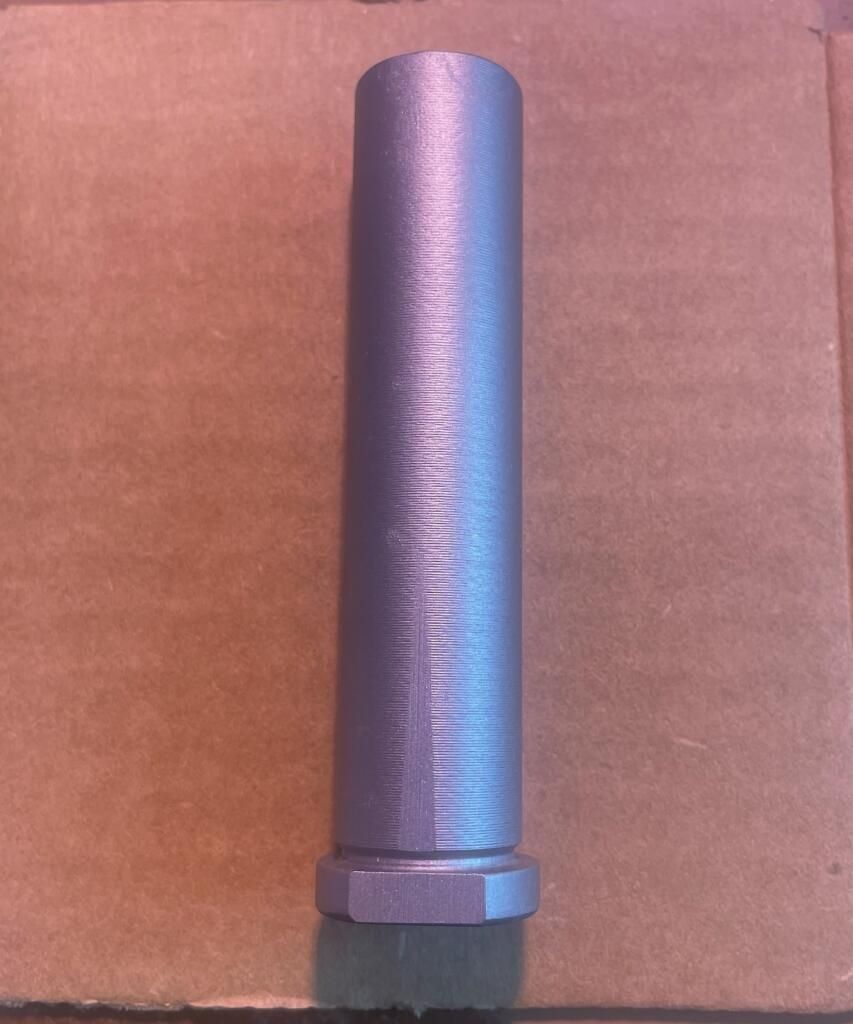 A cylindrical gray object with a hexagonal base, likely a metal part, on a brown surface.