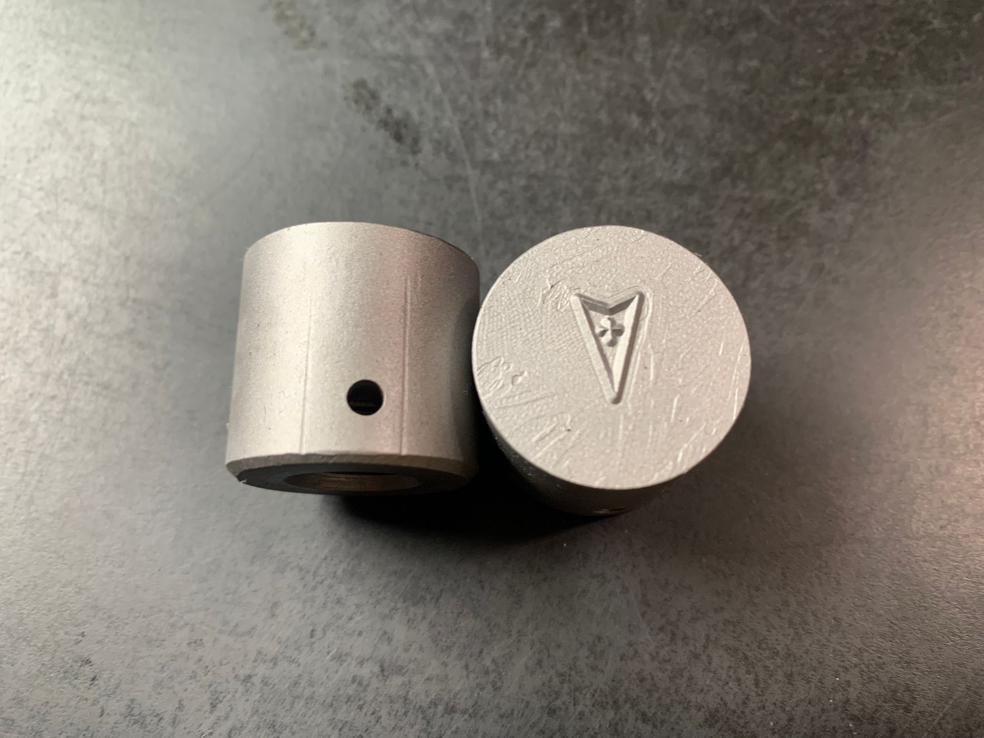 Two silver cylinders, one with a hole, the other with a Pontiac arrowhead logo.