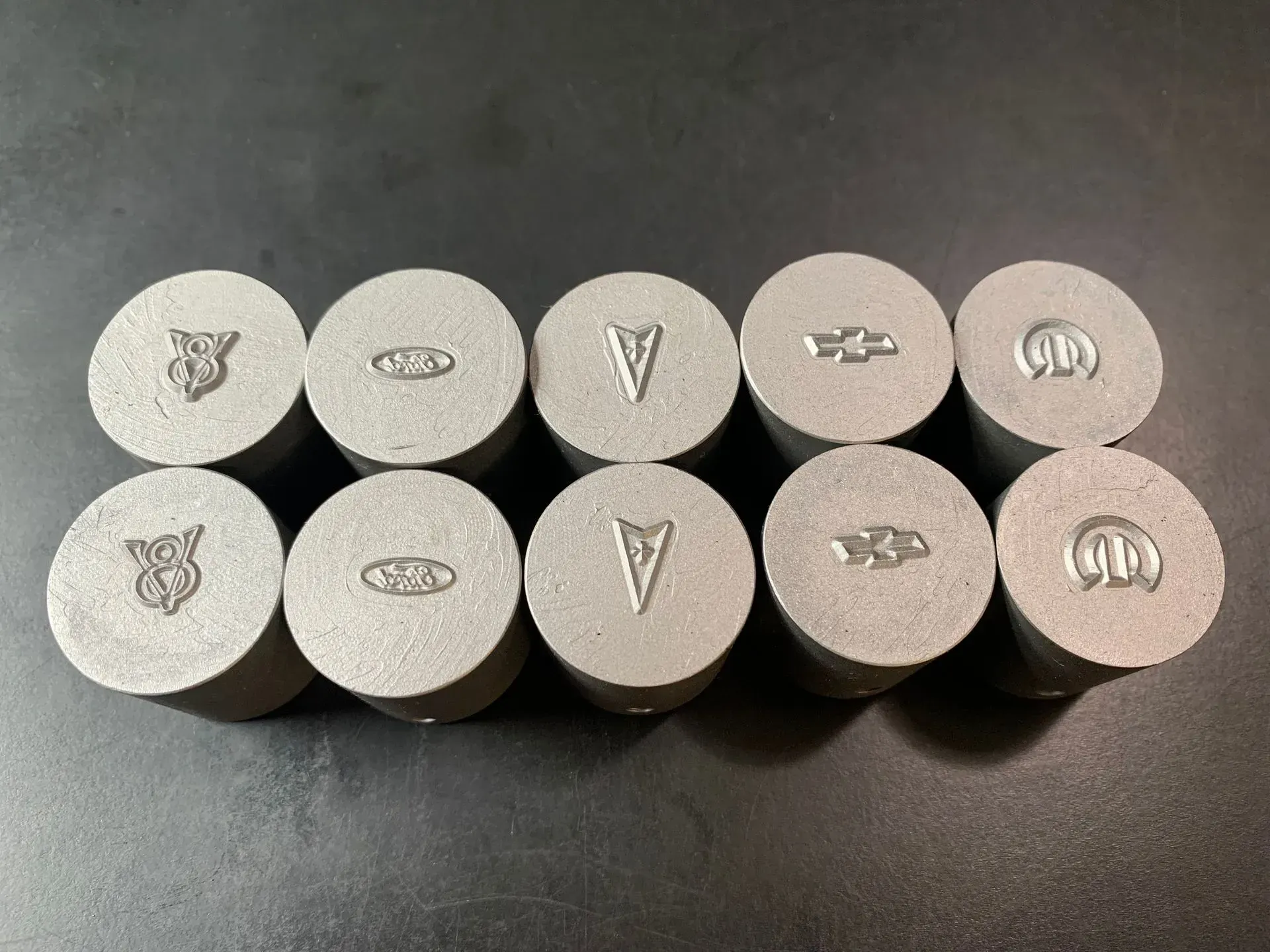 Ten silver metal caps, each with a different embossed car logo.