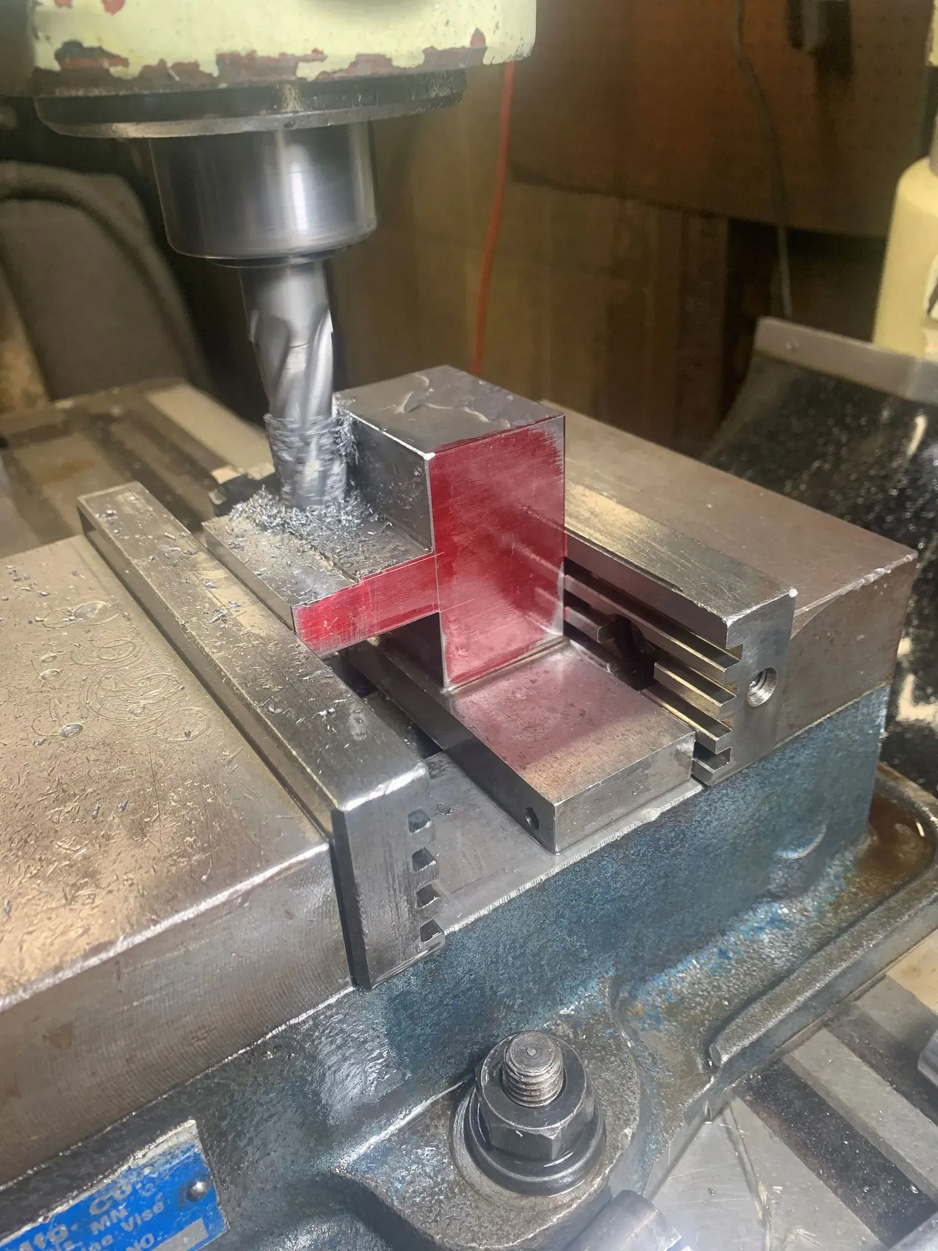 A metal milling machine in operation, cutting a red-marked metal part clamped in a vise.