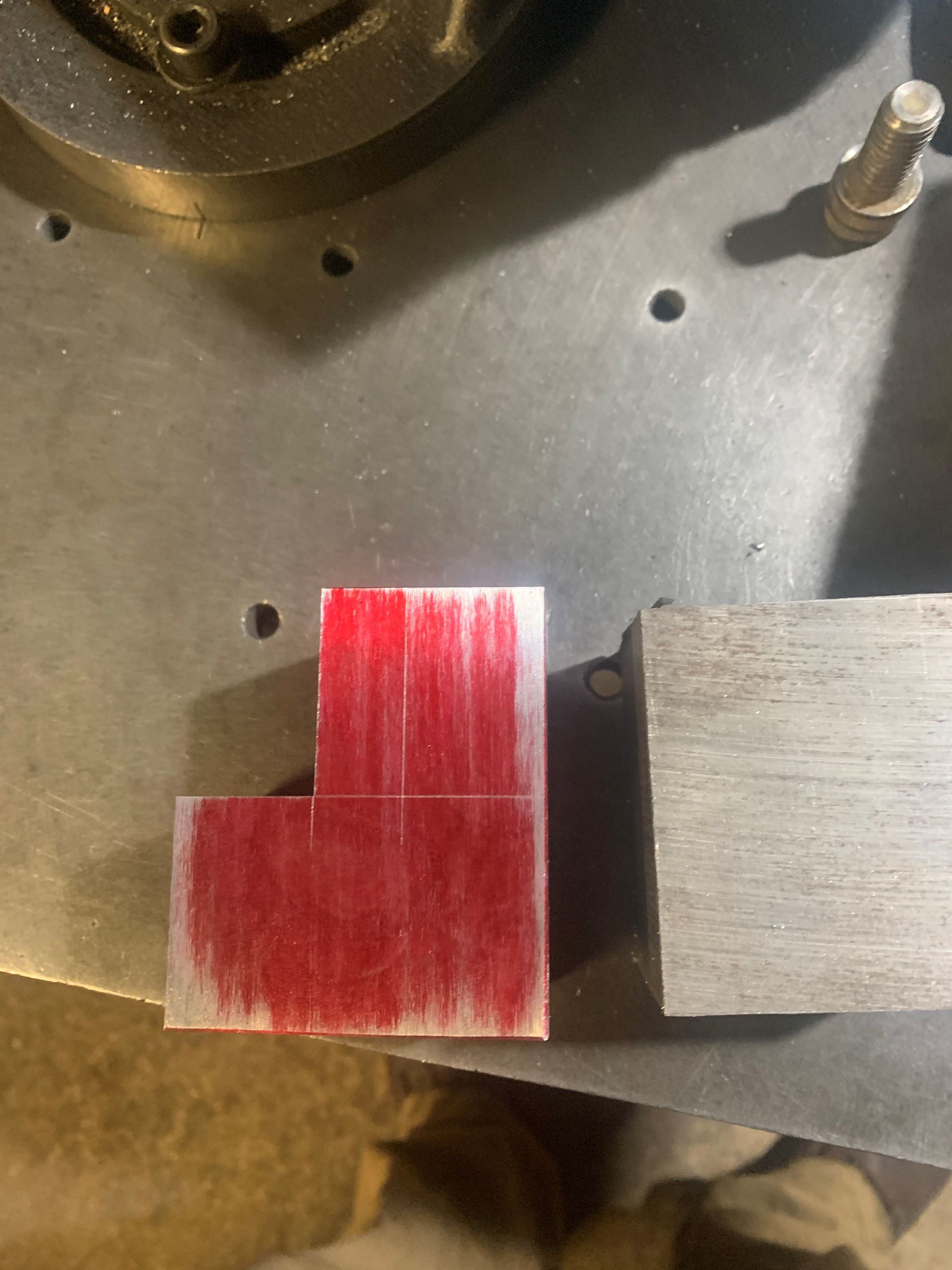 Red-marked metal L-shape and rectangular metal block on a gray surface, likely a workshop setting.