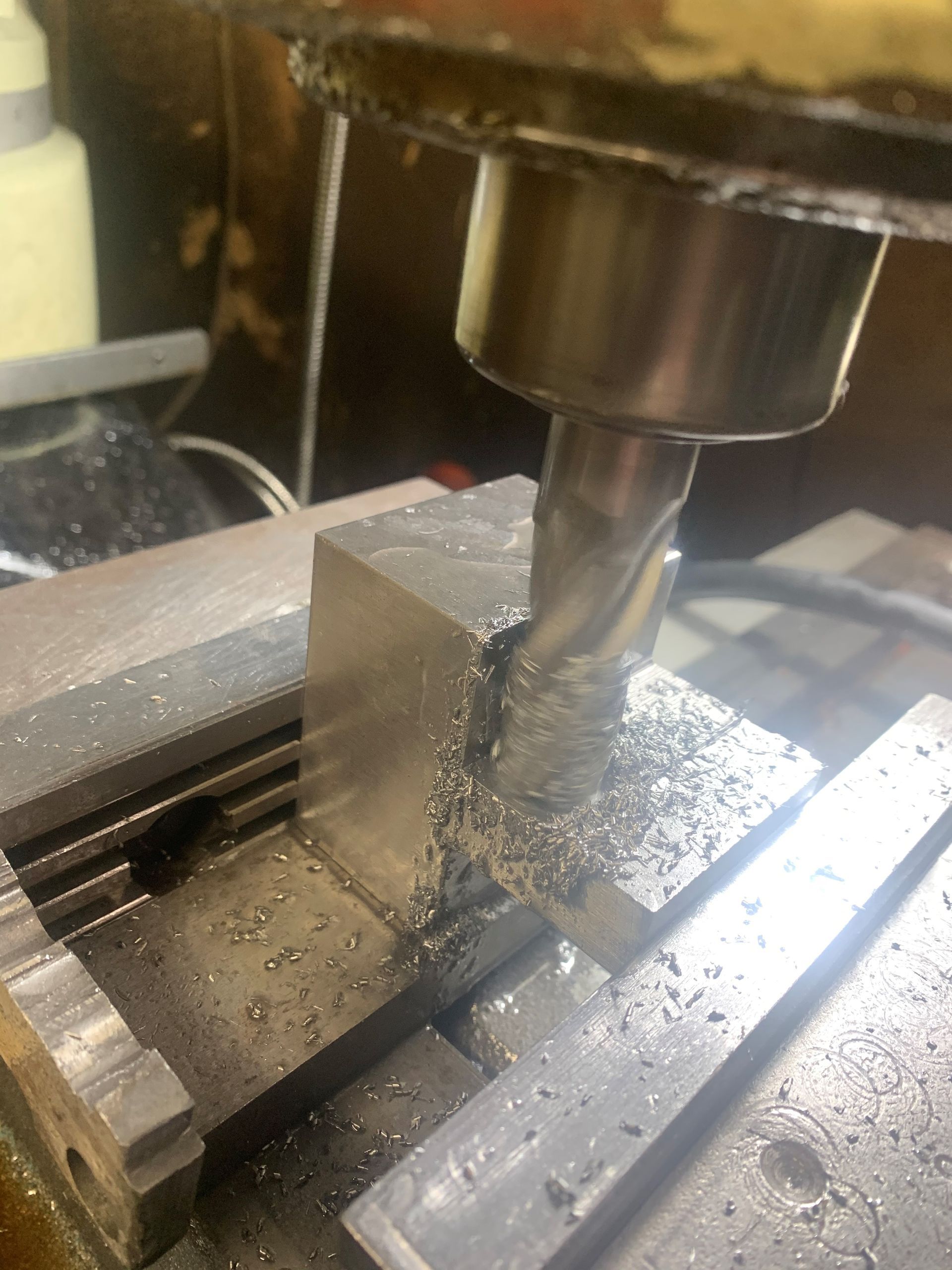 Milling machine cutting a metal block, generating metal shavings on a workshop table.
