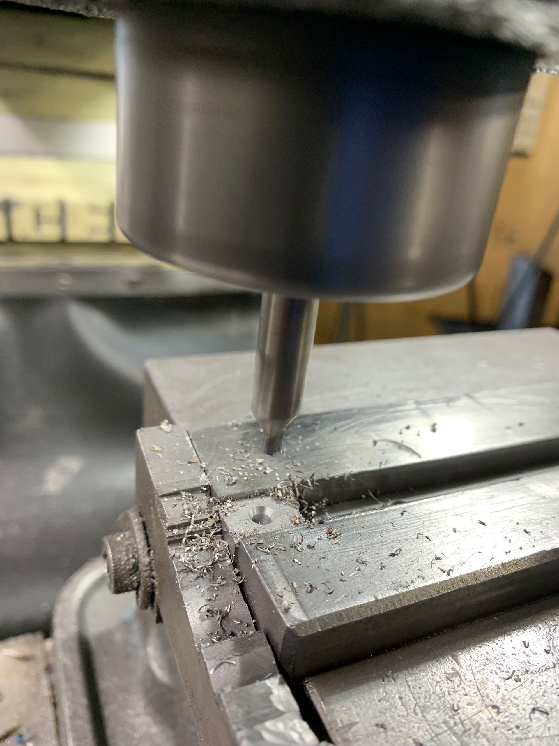 A milling machine cutting metal, creating chips. The cutting tool is near the corner of a metal block.