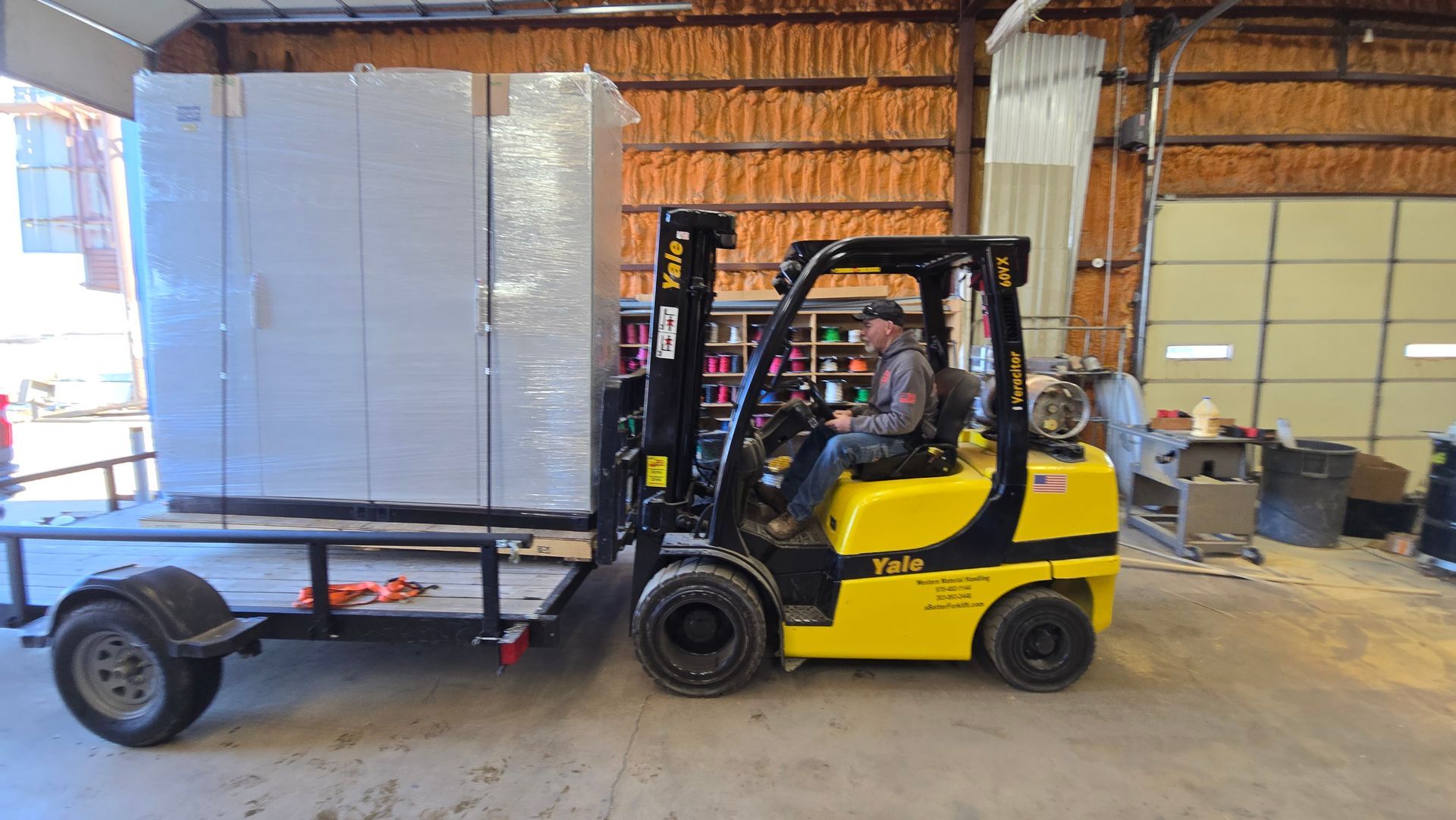 A man is driving a forklift in a garage next to a trailer.