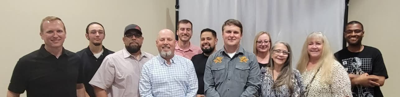 Group of diverse people smiling, standing indoors in front of a white curtain.
