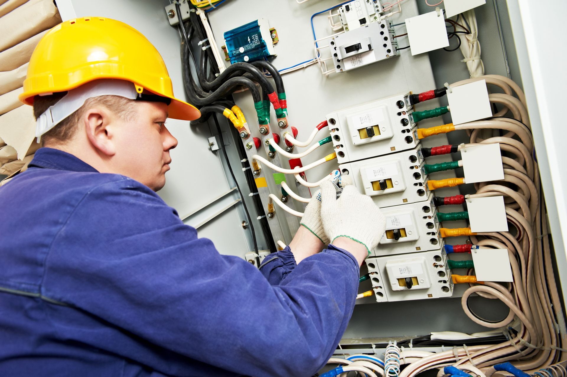 Electrician in yellow hard hat working on electrical panel.