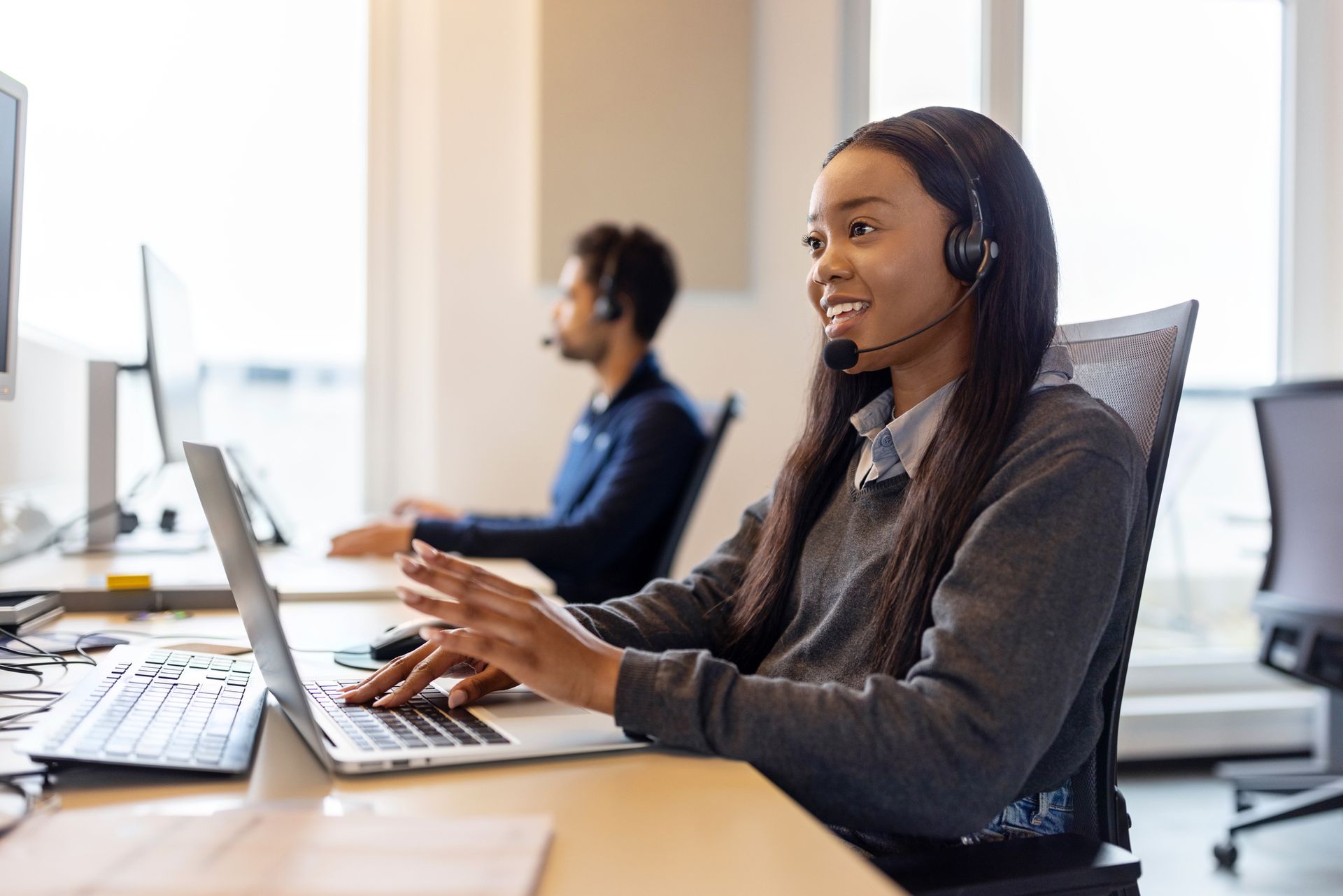 A woman wearing a headset is sitting at a desk using a laptop computer. - Plymouth, MN - Legacy Pro