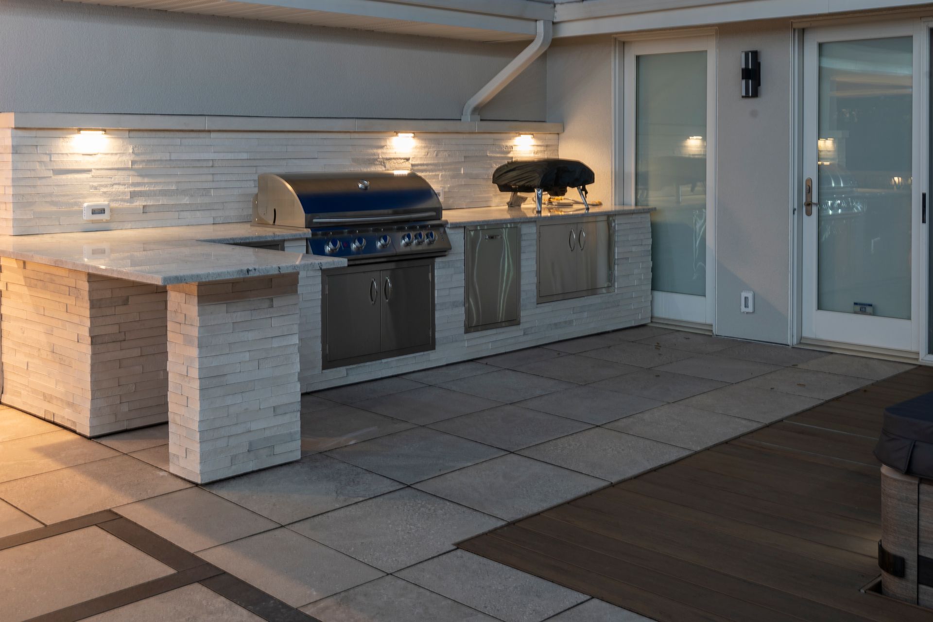 Outdoor patio with built-in grill and counter, tiled floor, and string lights at dusk
