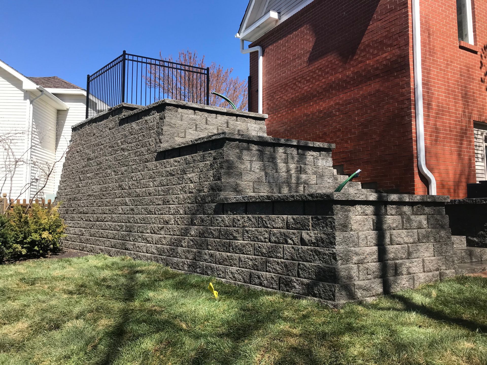 Stone retaining wall beside a house with a blue-railed deck and grassy yard under a clear sky
