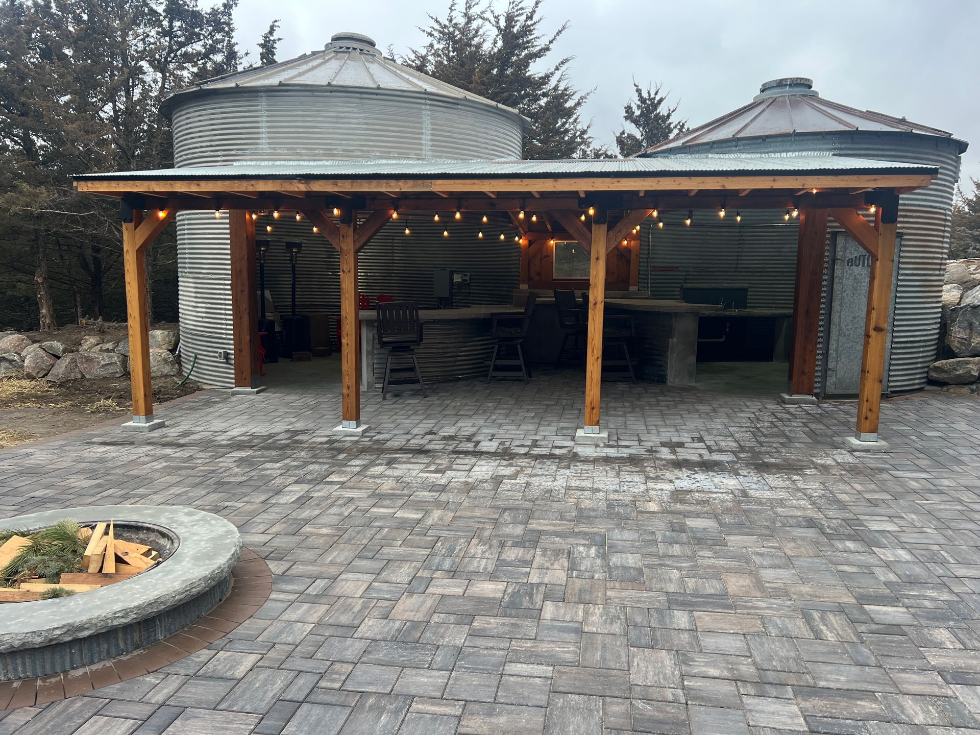Covered outdoor patio with string lights, wooden posts, and a stone paver courtyard at dusk