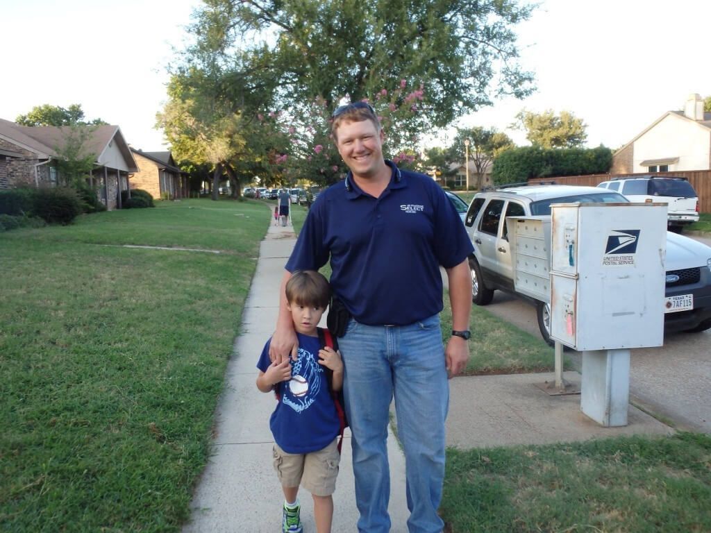 A man and a boy are standing on a sidewalk in front of a mailbox