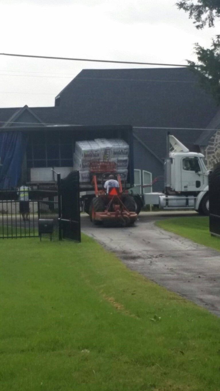 A truck is driving down a dirt road next to a house.