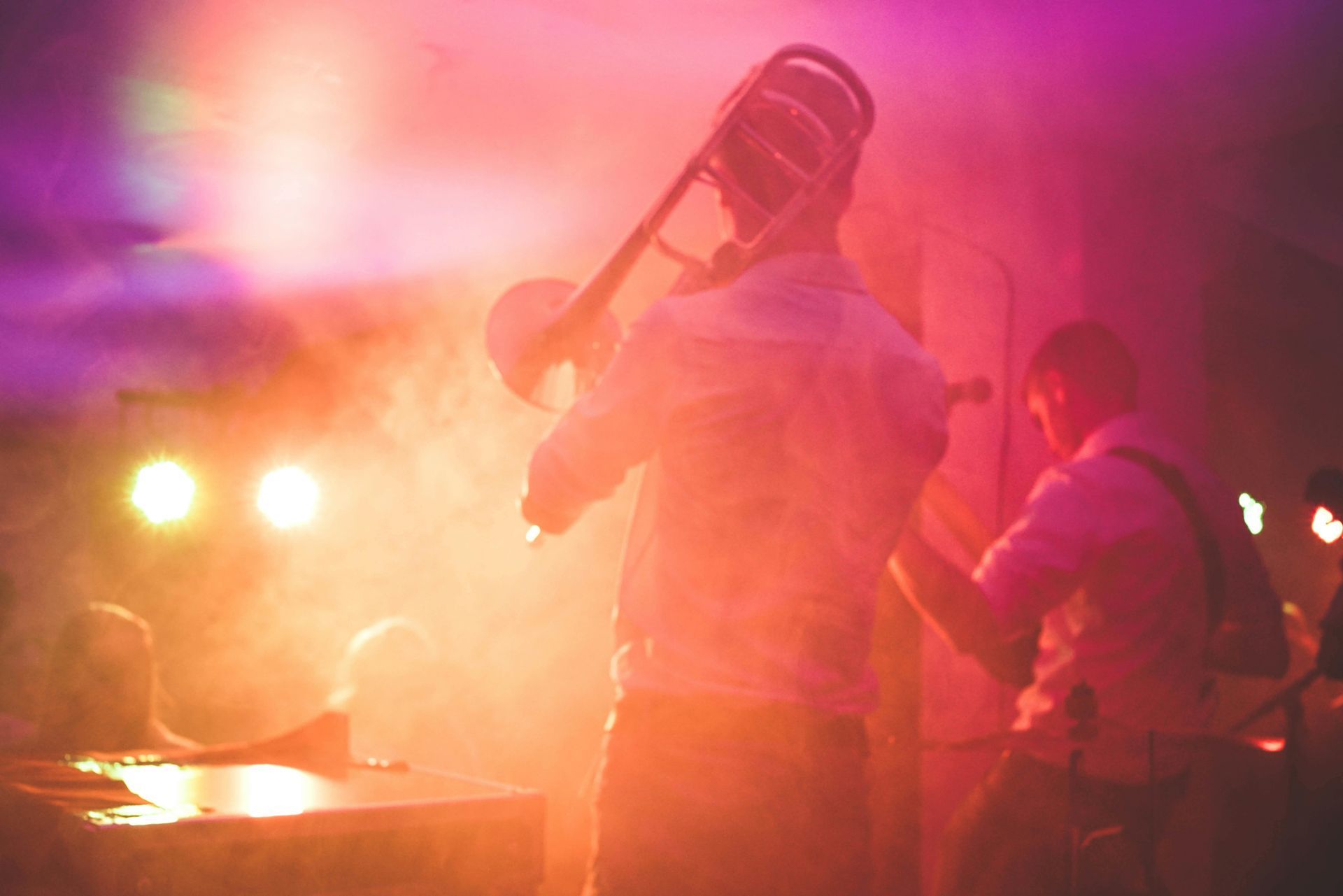 A musician playing a trombone on stage, illuminated by orange and purple lights.
