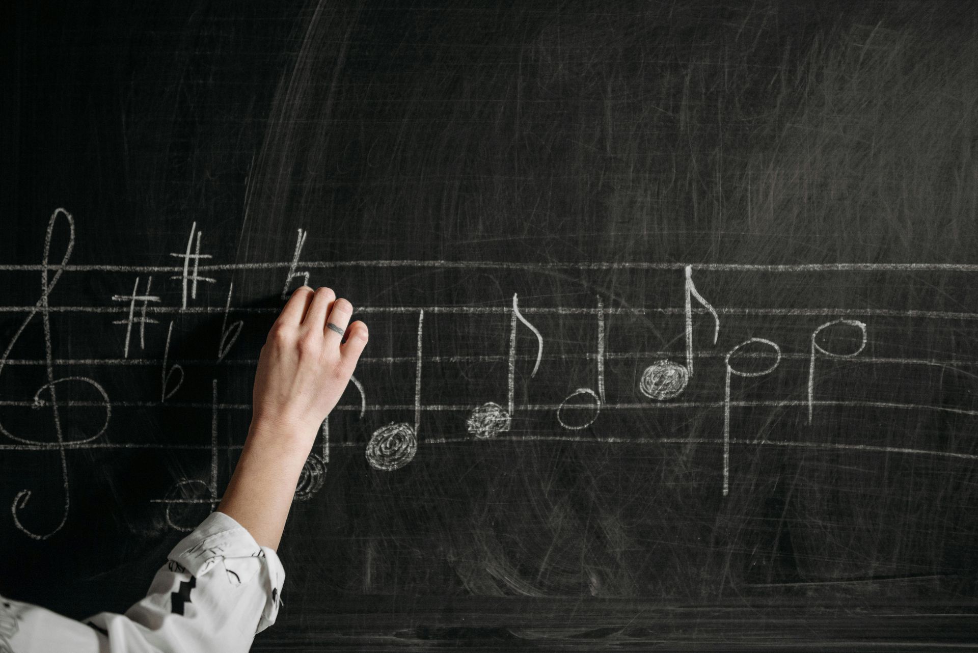 Hand writing musical notes with chalk on a chalkboard.