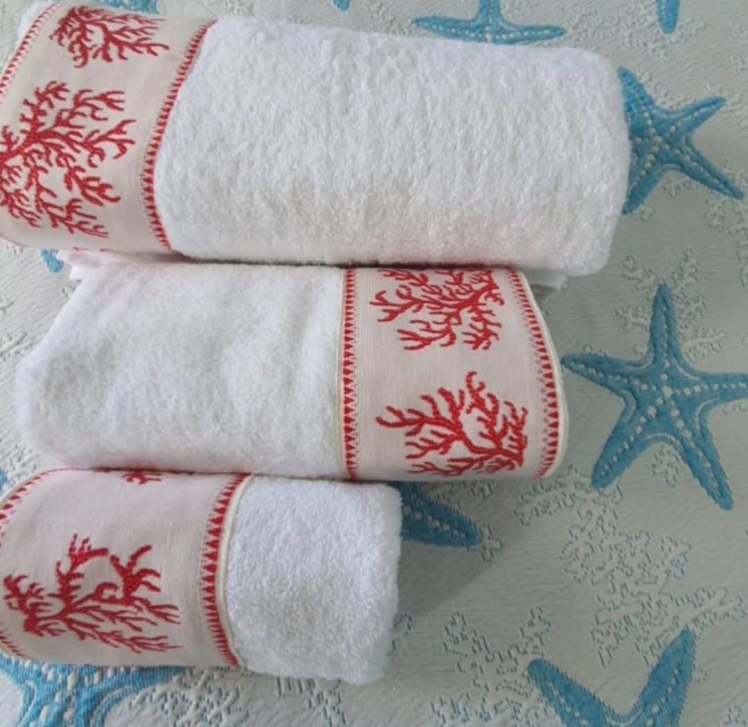 Tre asciugamani bianchi con coralli rossi sopra sono impilati uno sopra l'altro