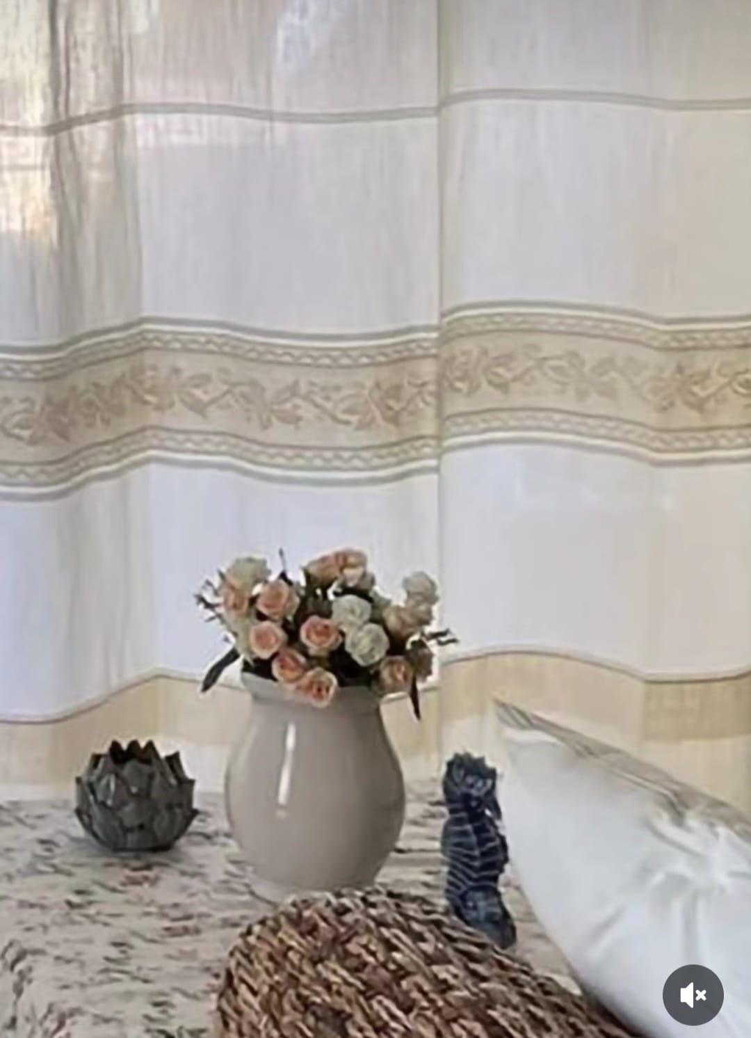 Un vaso di fiori è appoggiato su un tavolo davanti a una tenda bianca.