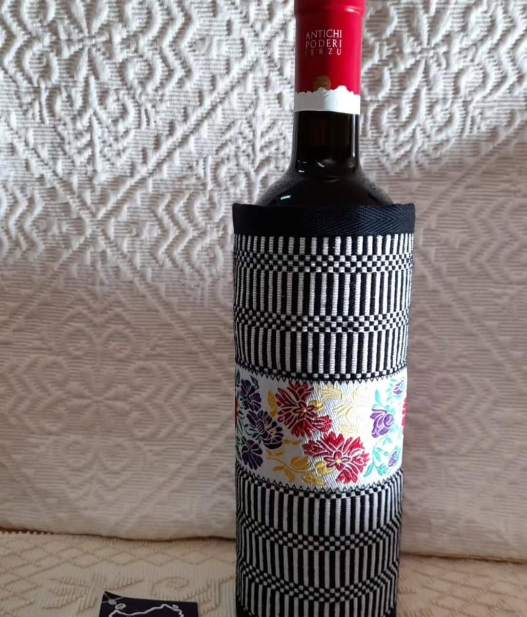 Una bottiglia di vino con una custodia a strisce bianche e nere è appoggiata su un tavolo.