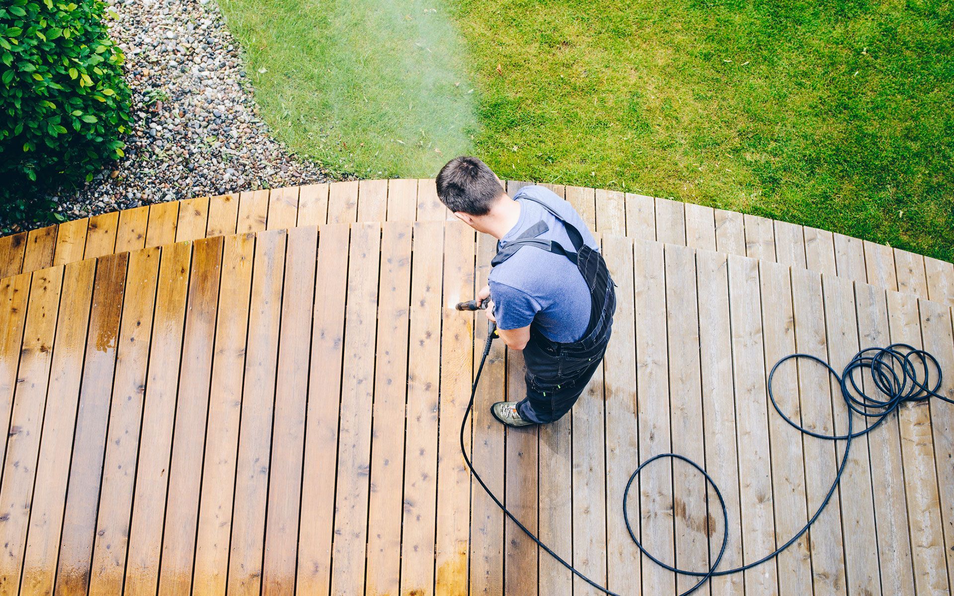 A man is cleaning a wooden deck with a high pressure washer.