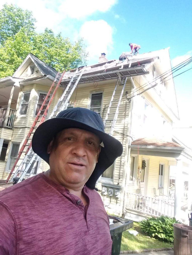 A man wearing a hat is standing in front of a house.