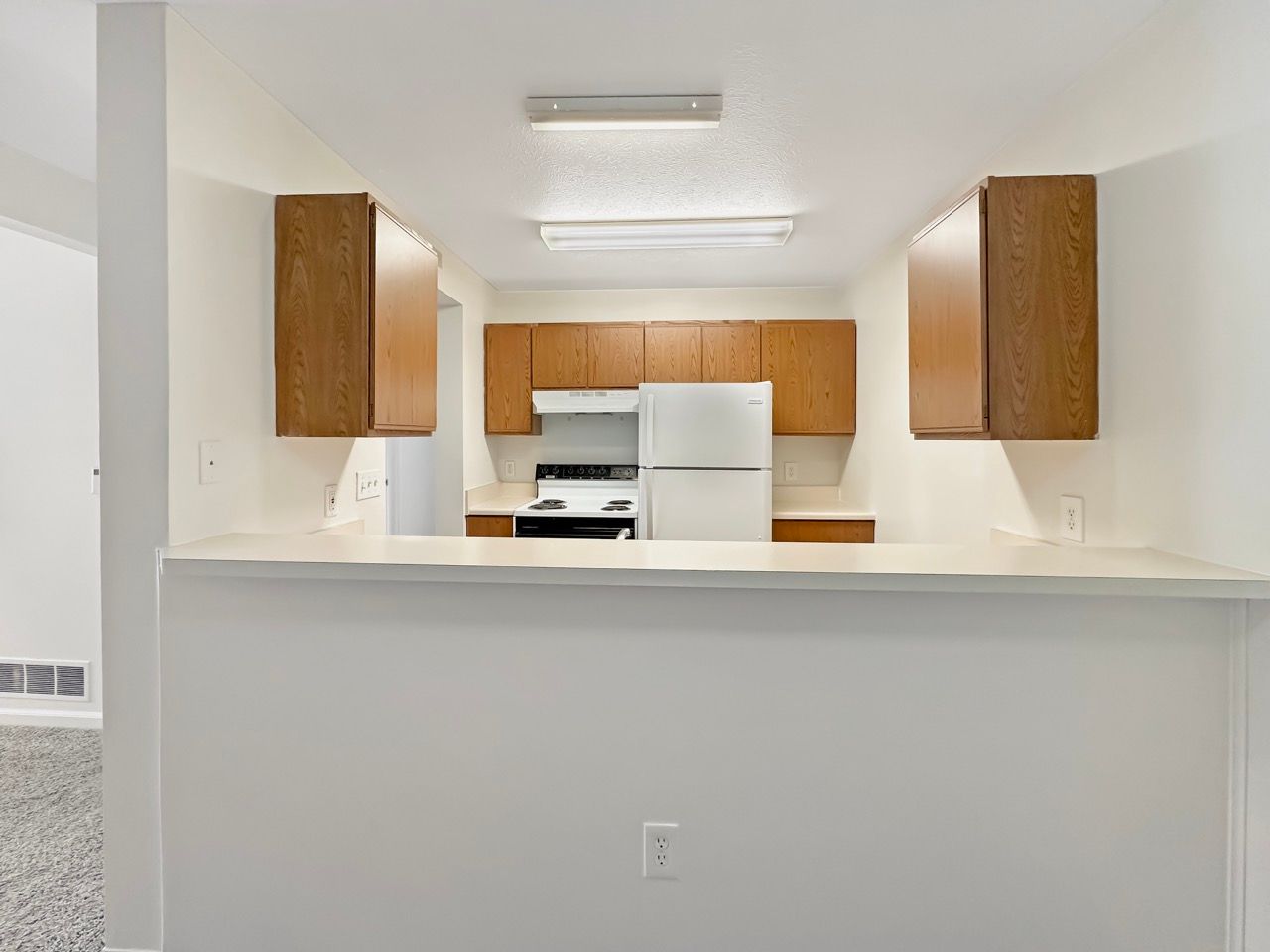 An empty kitchen with a refrigerator , stove , and cabinets.