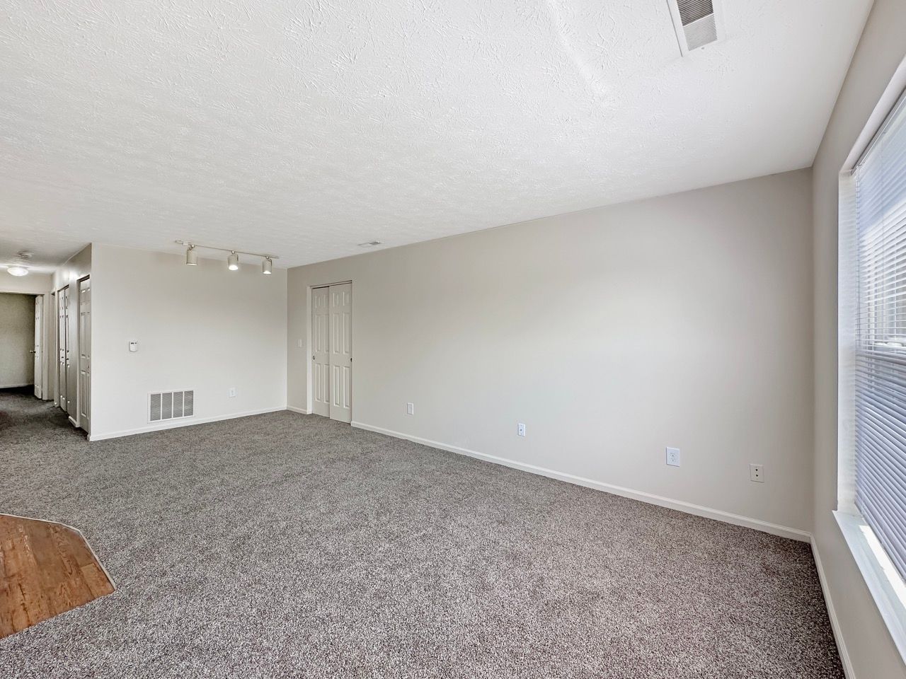 An empty living room with a carpeted floor and a window.