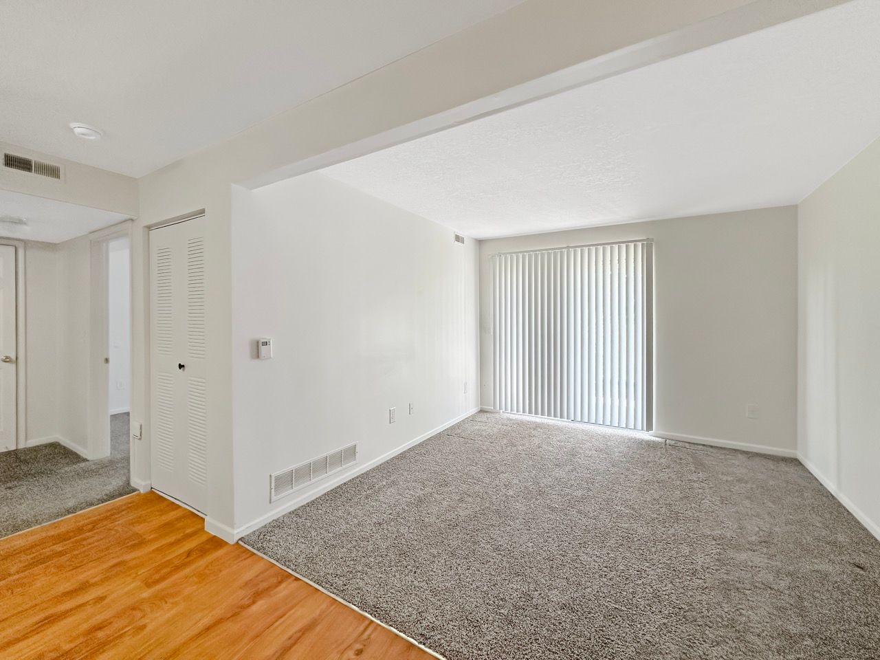 An empty living room with hardwood floors and a sliding glass door.