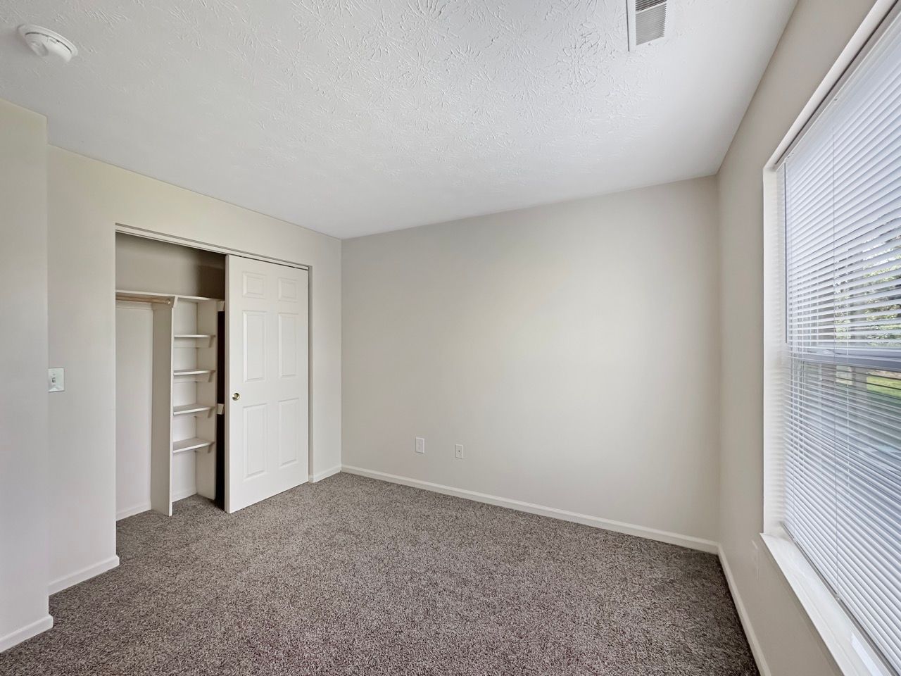 An empty bedroom with a window and a closet.