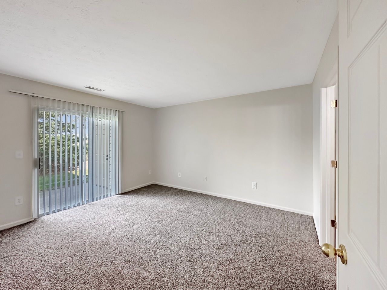 An empty living room with a sliding glass door and a carpeted floor.