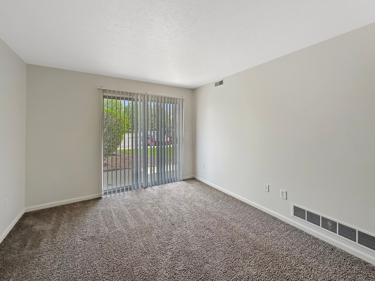 An empty living room with a sliding glass door and a carpeted floor.