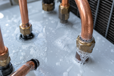 Copper pipes with brass fittings on a frosty metal surface, showing condensation or frost buildup.