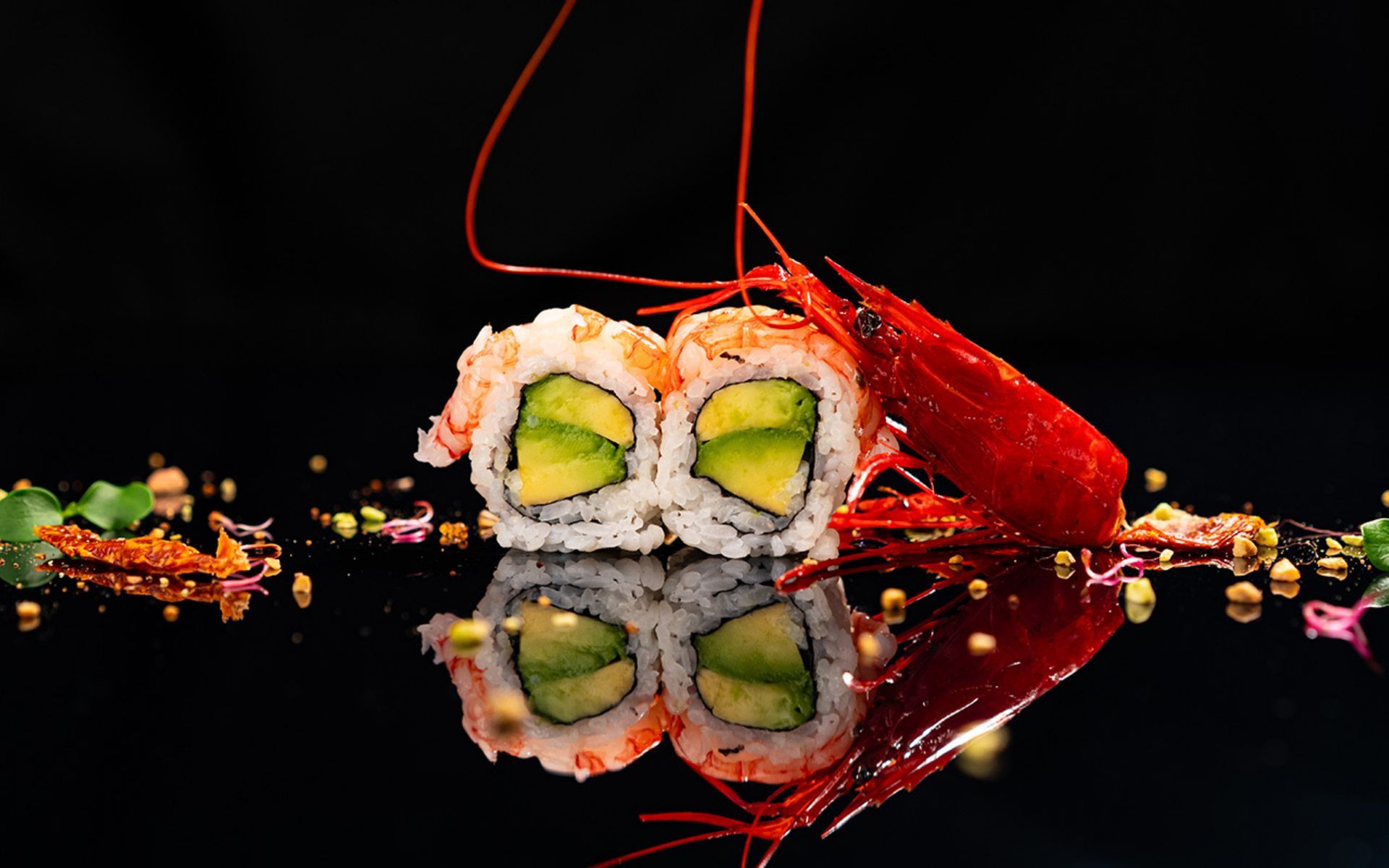 Involtini di sushi ripieni di avocado, guarnito con un gambero rosso.