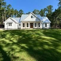 A white house is sitting on top of a lush green lawn surrounded by trees.