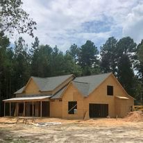 A house is being built in the middle of a dirt field surrounded by trees.