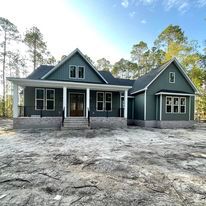 A green house with a porch is sitting on top of a dirt field.
