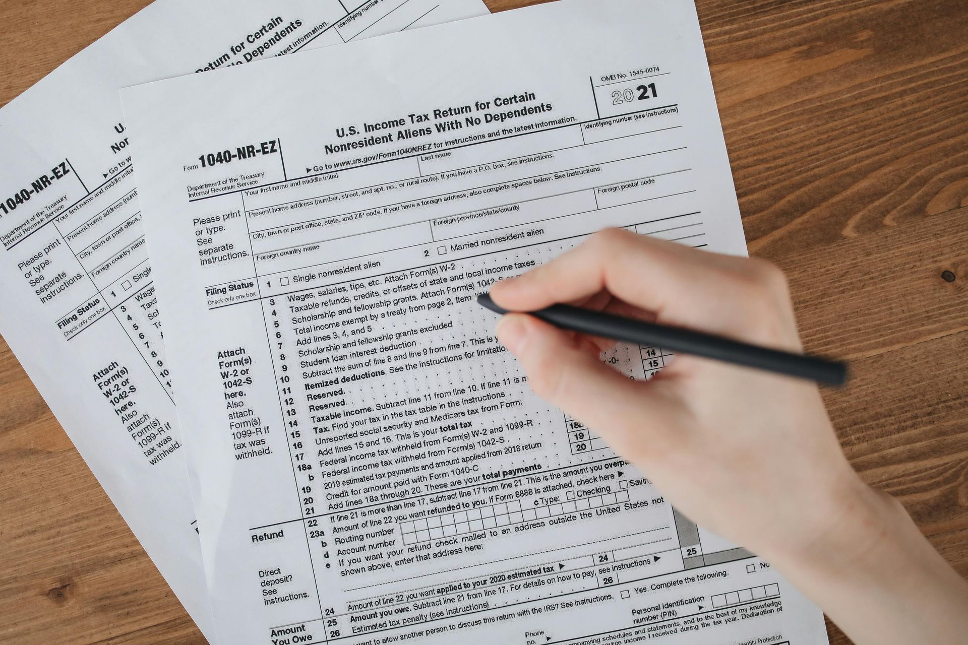 A hand holds a black pen, filling out a tax form on a wooden table.