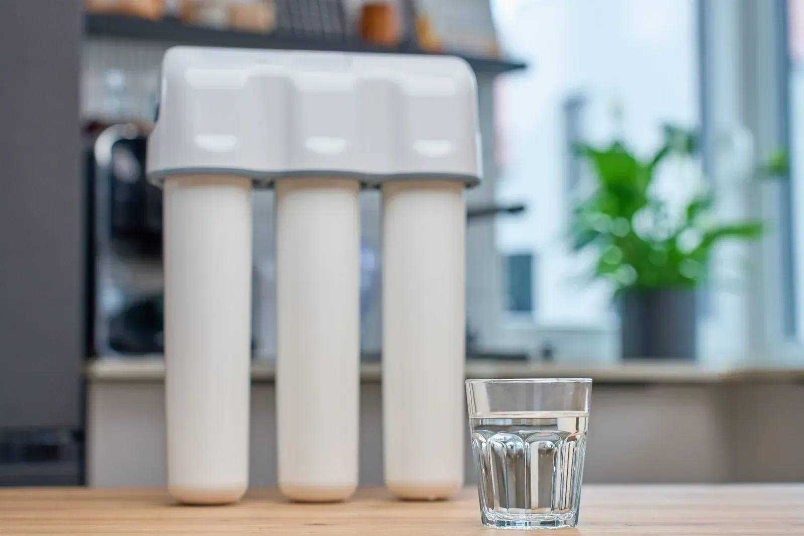 Water filter system with a glass of clear water on a wooden table.