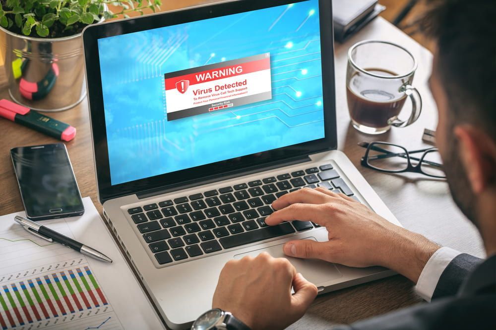 A Man Is Typing On A Laptop Computer With A Warning Sign On The Screen — Black Label I.T. in Garbutt, QLD