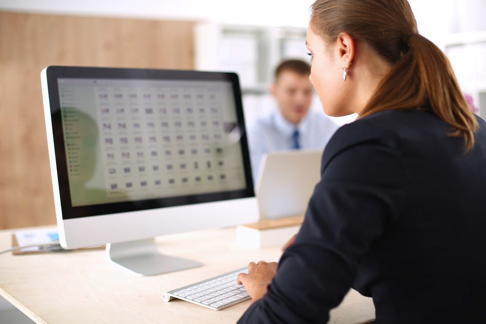 A Woman Is Sitting At A Desk Looking At A Computer Screen — Black Label I.T. in Garbutt, QLD
