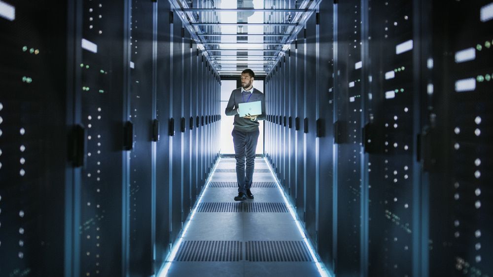 A Man Is Walking Through A Server Room Holding A Laptop — Black Label I.T. in Garbutt, QLD