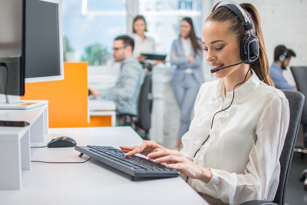 A Woman Wearing Headphones Is Typing On A Keyboard In A Call Center — Black Label I.T. in Garbutt, QLD