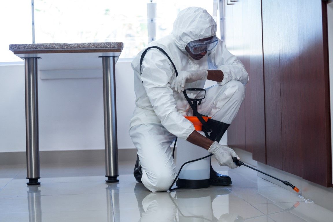 Worker in white protective suit using a sprayer to clean a shiny floor indoors