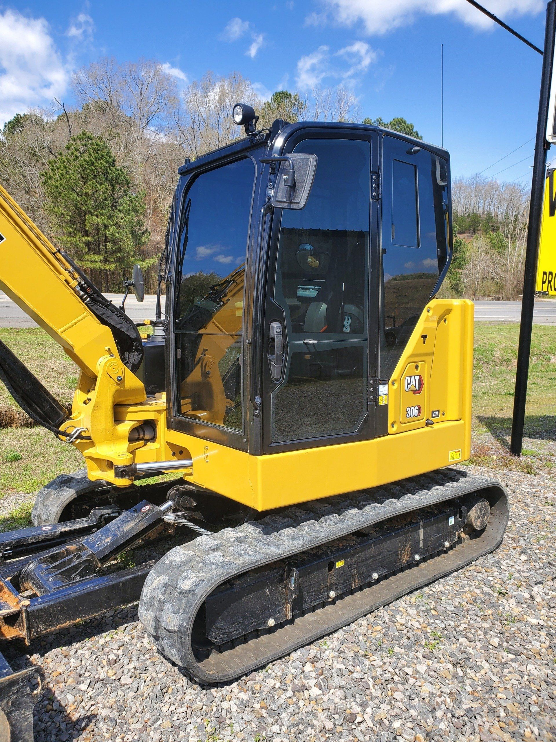 A small yellow excavator is parked on gravel next to a sign.
